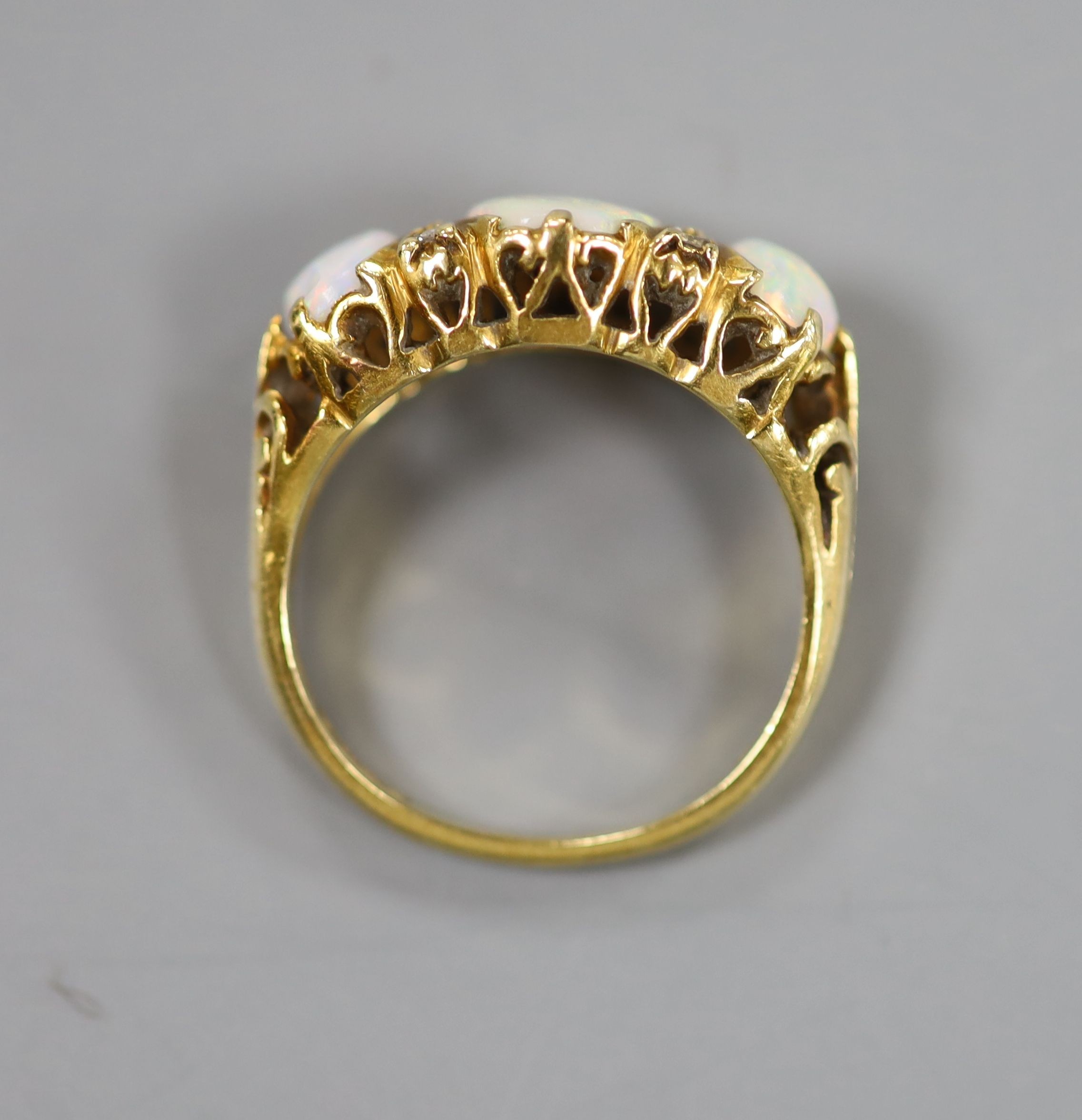 A 1970's Victorian style 18ct gold and graduated three stone white opal half hoop ring, with diamond chip spacers, size N, gross weight 5.9 grams.